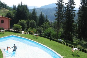 Une piscine où un homme et un enfant jouent, entourés d’une pelouse bien entretenue et d’arbres.