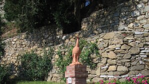 A stone wall with a statue of a bird on top, a brick pillar with a sign, and pink flowers growing against the wall. - Agriturismo la Torre (Bagni di Lucca)