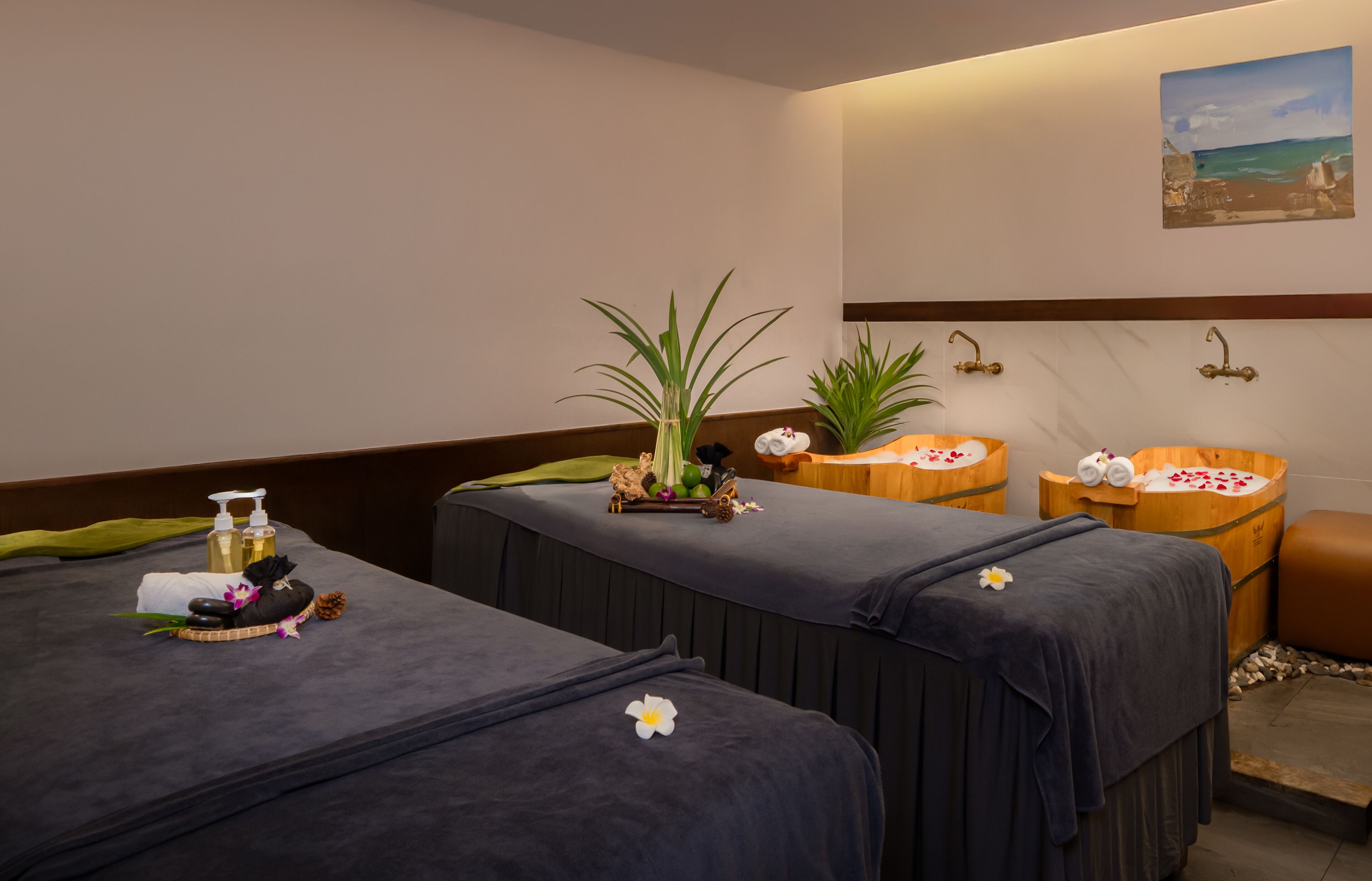 A spa room with two massage tables, a wooden tub, and a wall-mounted painting.