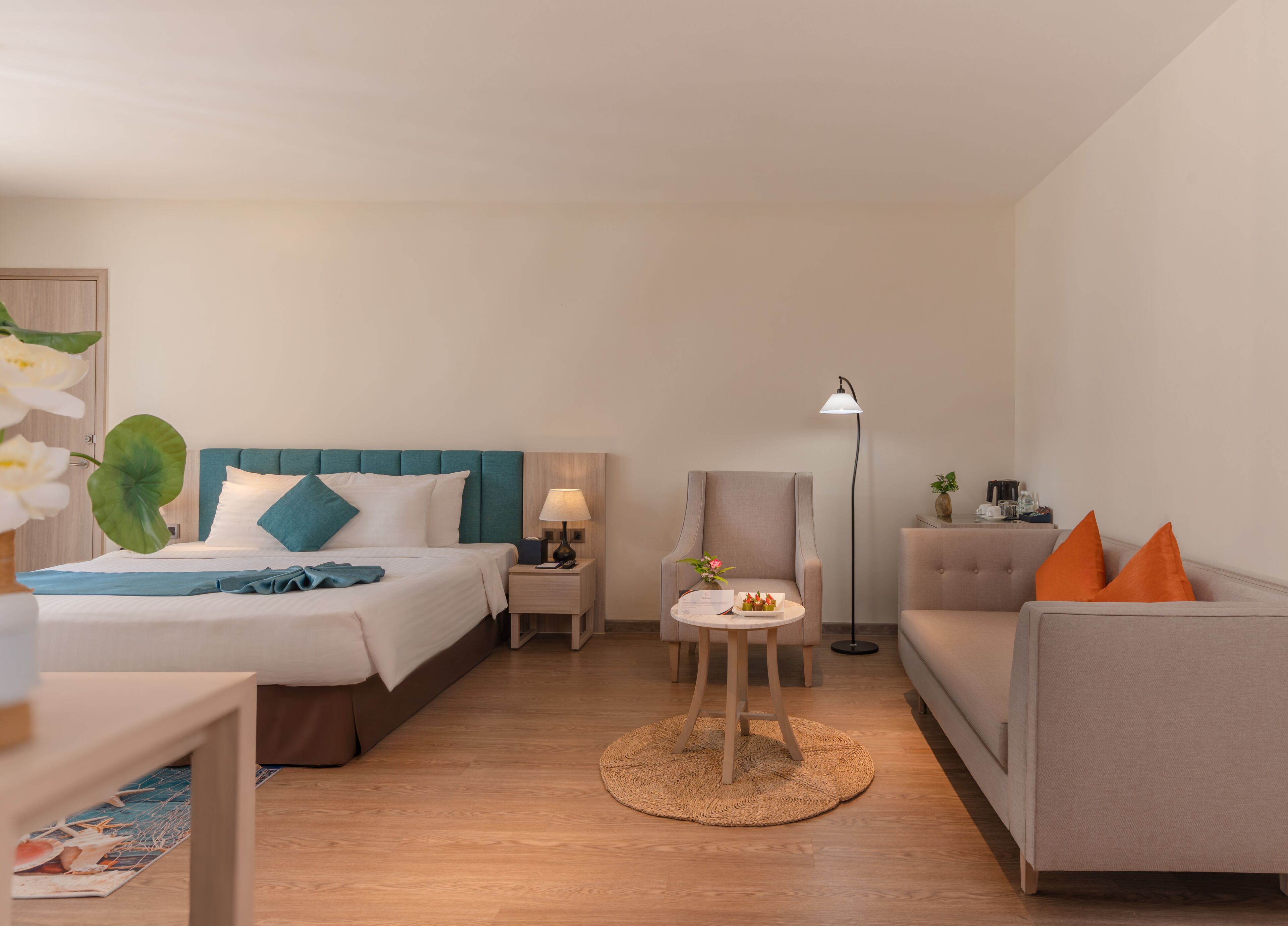 A hotel room with a bed, a sofa, a small table, and a floor lamp.