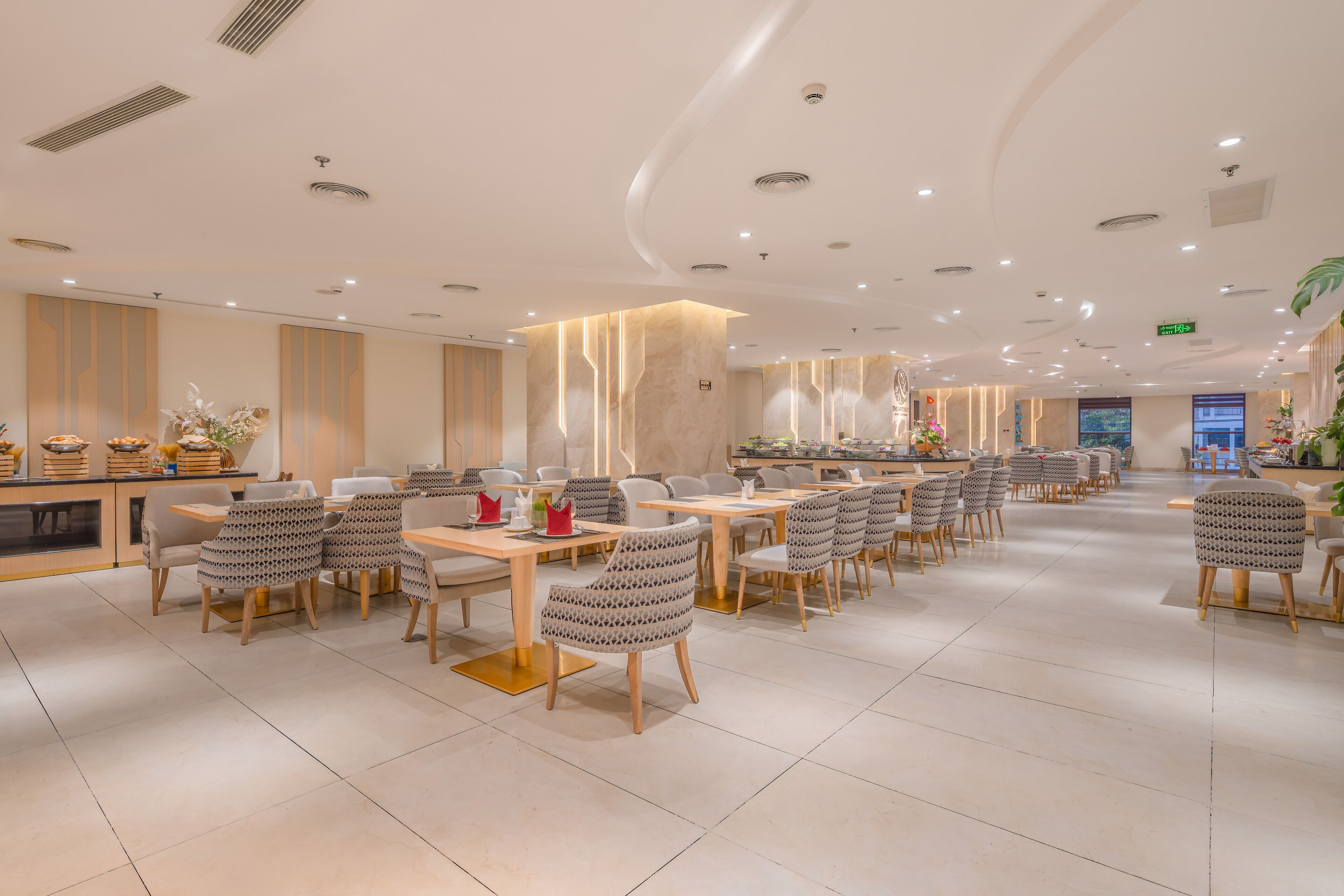 A spacious dining area with multiple tables and chairs, a counter with food items, and a modern ceiling design.
