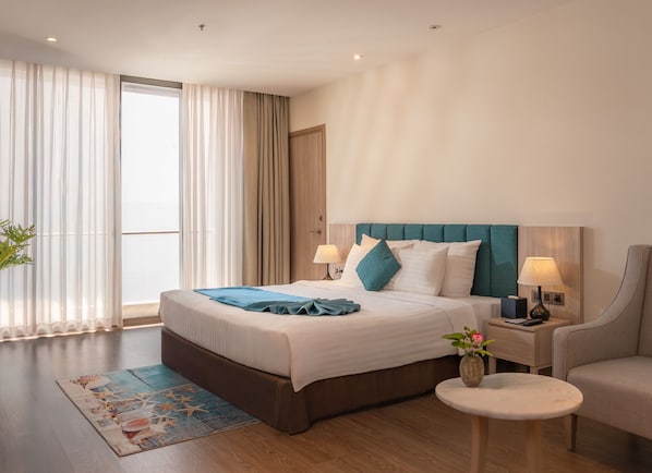 A modern hotel room with a large bed, a nightstand with a lamp, a round table, and a chair.