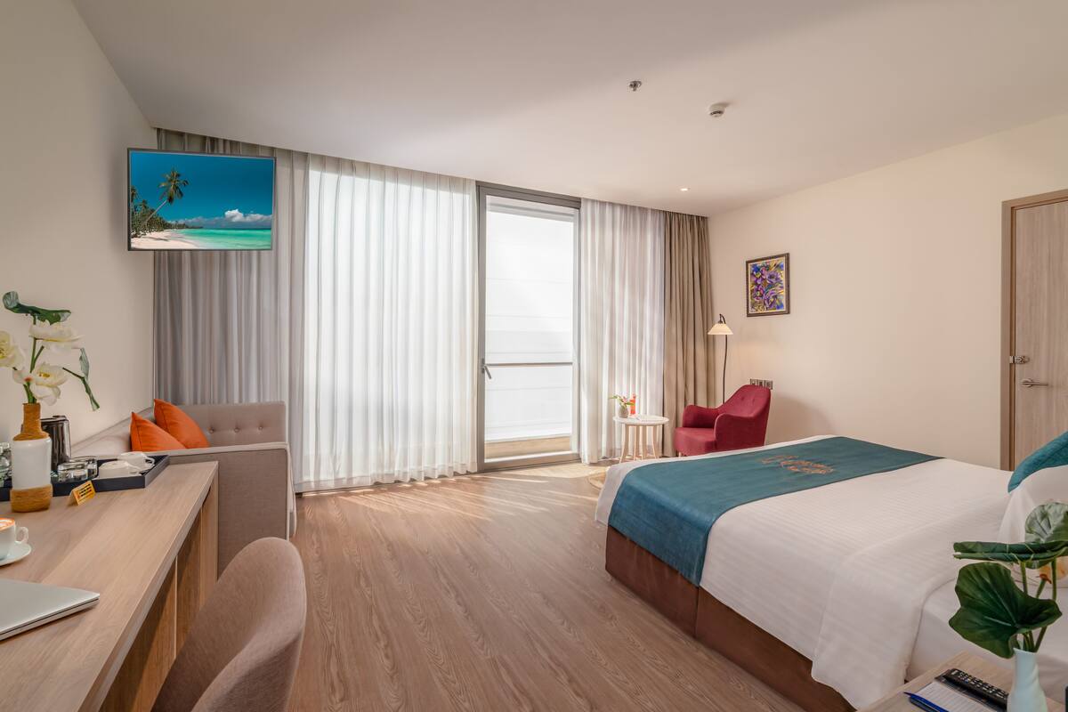 A hotel room with a bed, a desk, a chair, a TV, and a balcony.