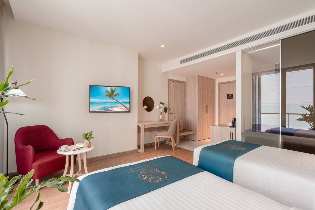 A hotel room with two beds, a desk, a chair, and a red armchair.