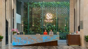 A hotel reception area with a marble reception desk, a glass wall with greenery, and a ceiling with a light fixture.