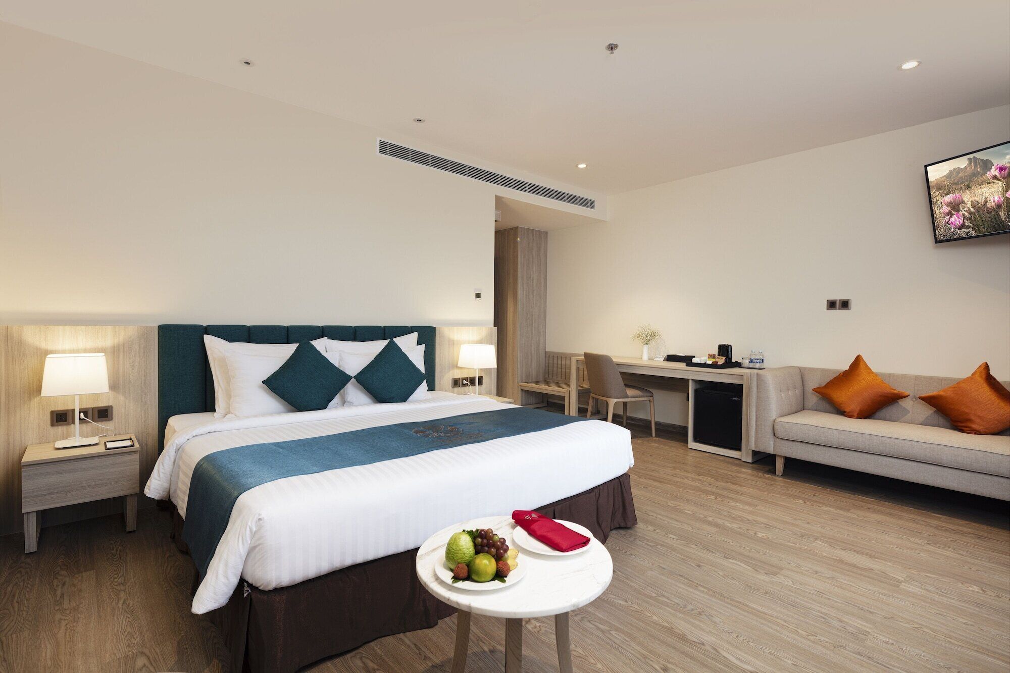 A hotel room with a bed, a desk, a sofa, and a small table with fruit.