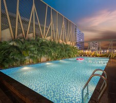 A swimming pool with a checkered tile pattern, surrounded by palm trees and a modern building with a unique architectural design.