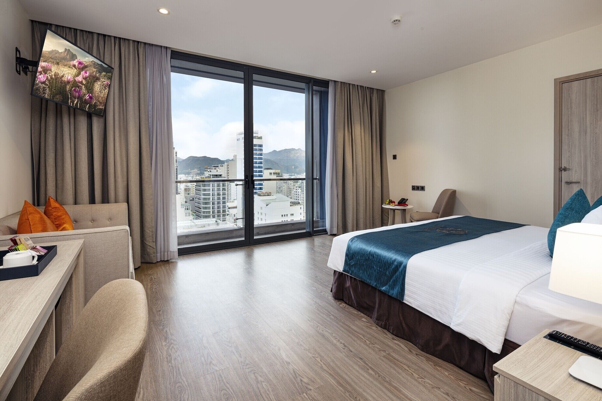 A modern hotel room with a large bed, a desk, a chair, and a balcony with a city view.