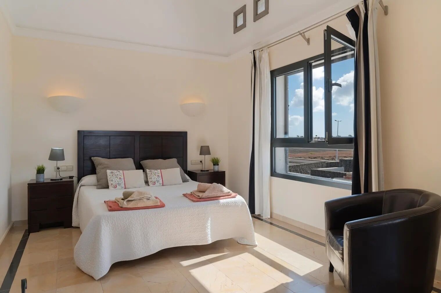Une chambre d’hôtel avec un grand lit, deux tables de chevet avec des lampes, une chaise et une fenêtre donnant sur un paysage.