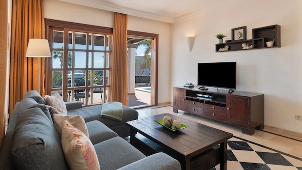 A modern living room with a sofa, coffee table, TV, and a view of the outdoors.