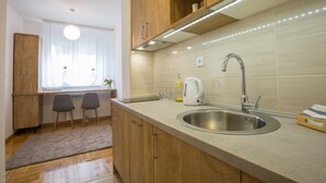 Una cocina moderna con armarios de madera, un lavamanos de acero inoxidable y una ventana con cortinas traslúcidas.