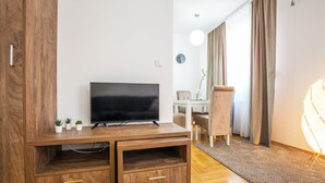 Una sala de estar moderna con un televisor de pantalla plana sobre un mueble de madera, un comedor con mesa y sillas, y un ventanal con cortinas.
