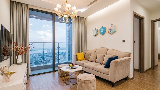 A modern living room with a large window, a sofa, a coffee table, and a chandelier. - Shendo Vinhomes Metropolis (Hanoi)