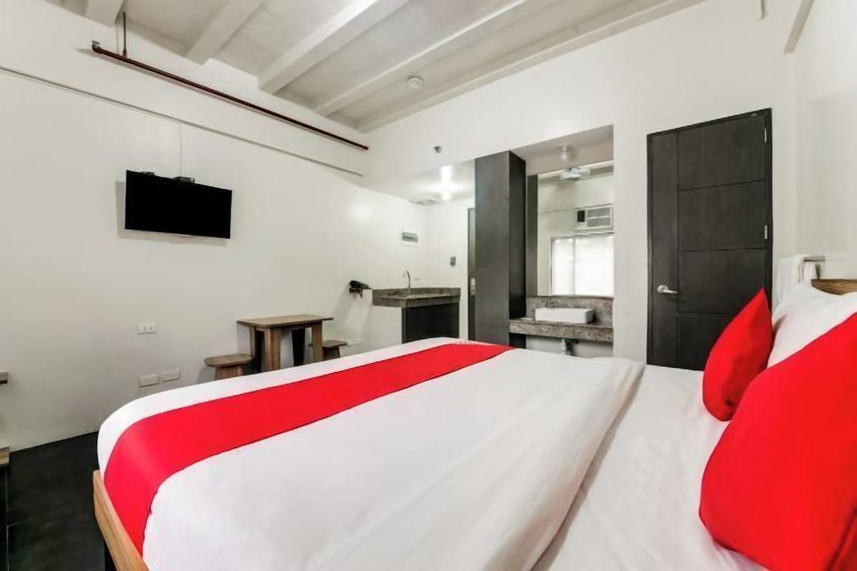 A hotel room with a bed, a TV, a mirror, a door, and a small table.