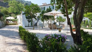 A courtyard with outdoor seating, a gravel path, and a building with green shutters. - Bed & Breakfast Il Casale di Monserrato (Porto Azzurro)