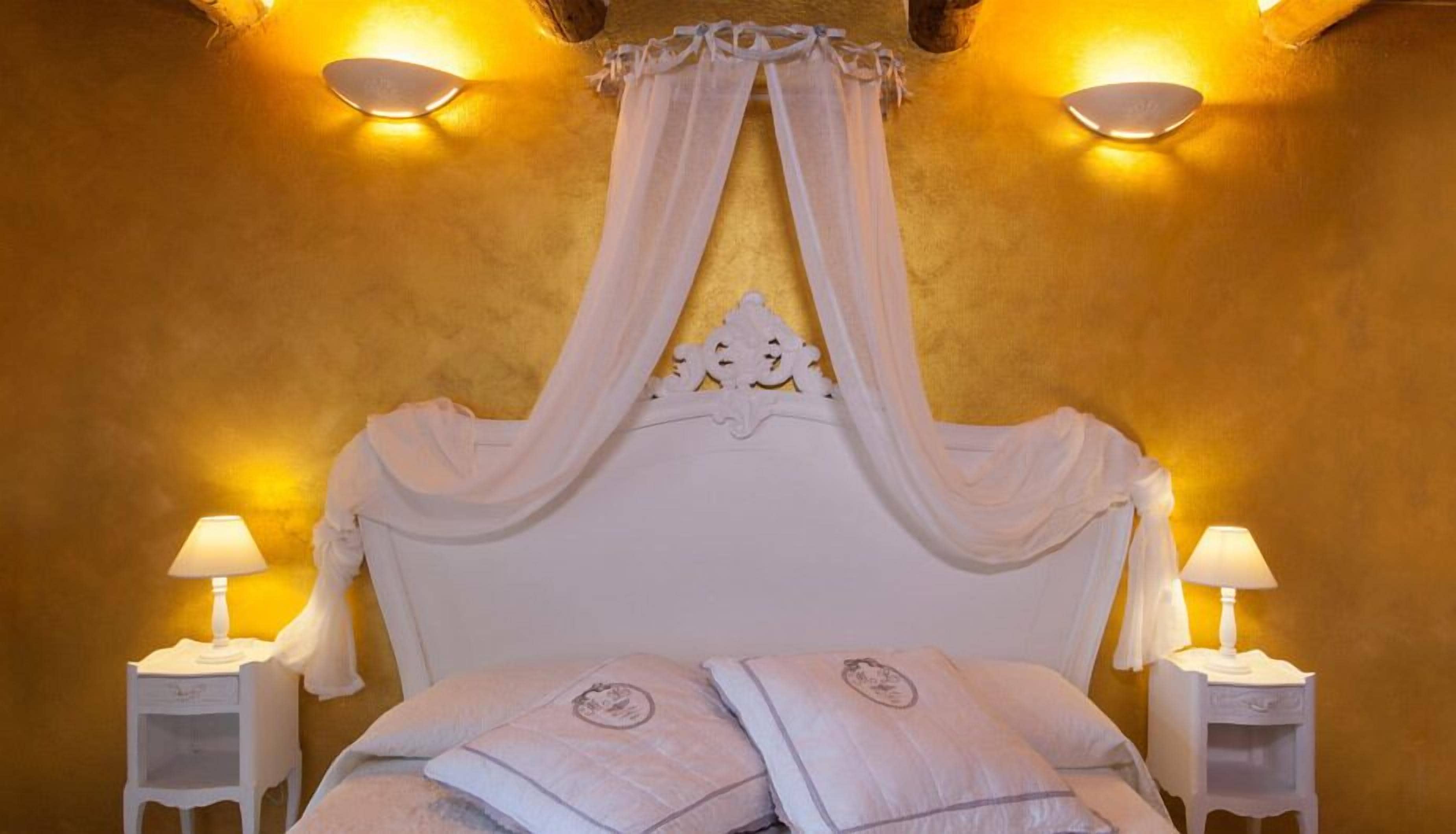 Een bed met hemel, twee bedlampen en een decoratief hoofdbord.