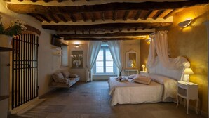 A bedroom with a bed, bedside tables, a window with curtains, a mirror, and a small seating area with a sofa. - Bed & Breakfast Il Casale di Monserrato (Porto Azzurro)