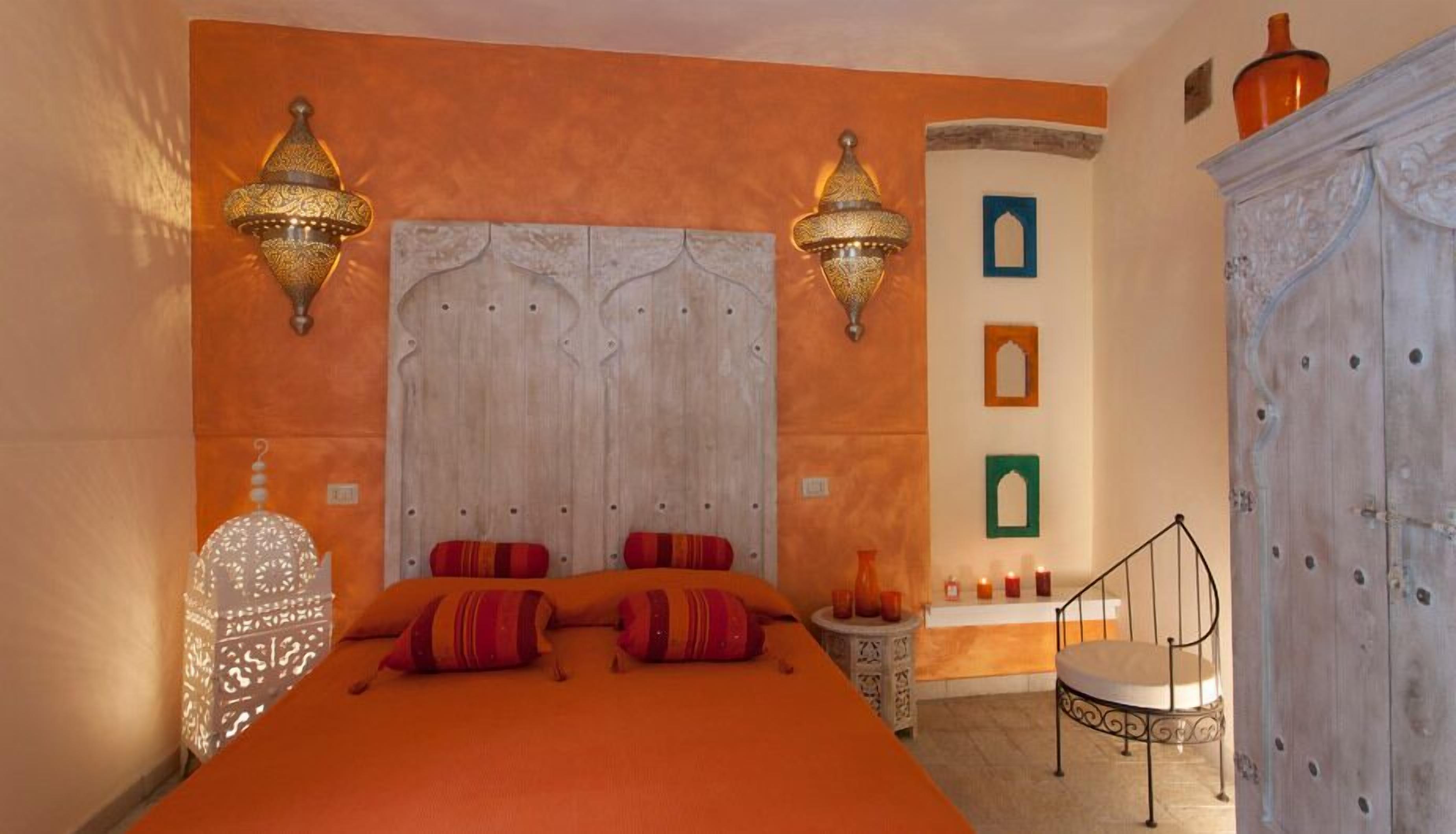 A bedroom with a large bed, two wall-mounted lamps, a nightstand, and a chair.