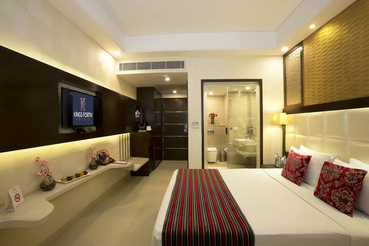 A hotel room with a bed, a TV, a bathroom, and a reception desk.