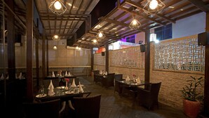 An outdoor dining area with tables and chairs, a wooden ceiling, and a brick wall with a lattice design. - Kings Forth Hotels (New Delhi)
