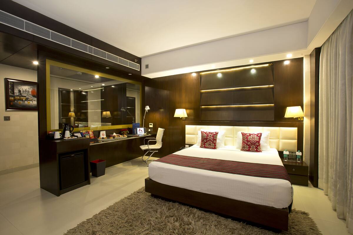 A modern hotel room with a large bed, a desk with a mirror, and a small seating area.