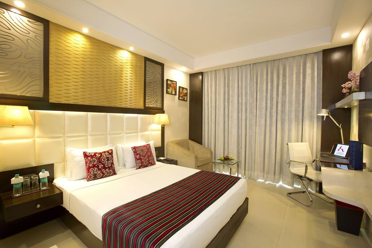 A hotel room with a large bed, a desk, a chair, a nightstand, and a lamp.
