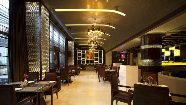 A modern dining area with high ceilings, chandeliers, and a view through large windows. - Kings Forth Hotels (New Delhi)