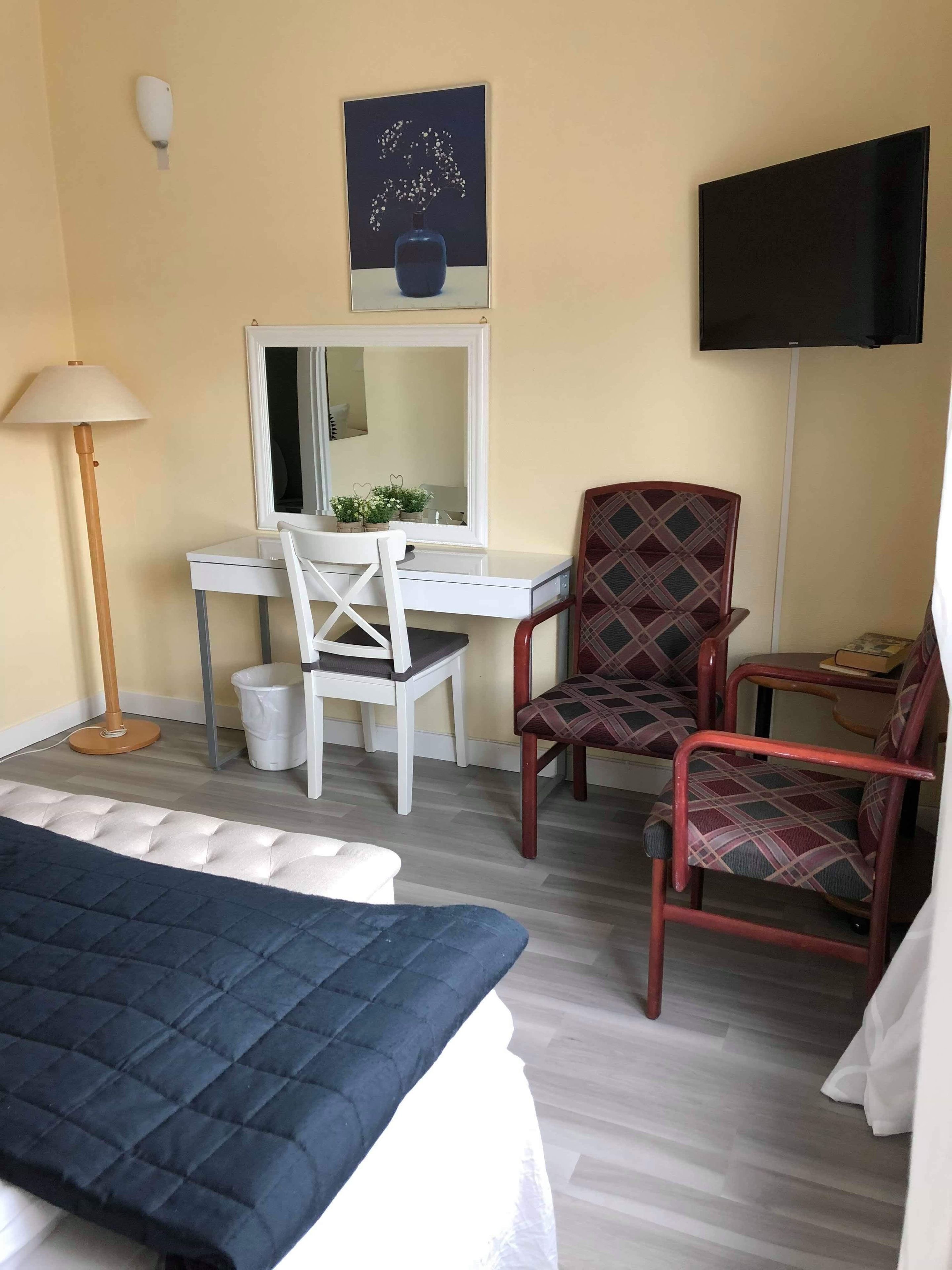 Habitación de hotel con cama, escritorio, dos sillas, televisor y espejo.