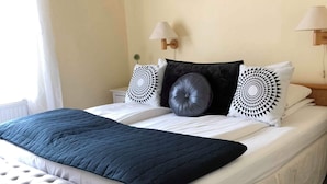 A neatly made bed with a dark blue quilt, two decorative pillows, and a bench at the foot of the bed.