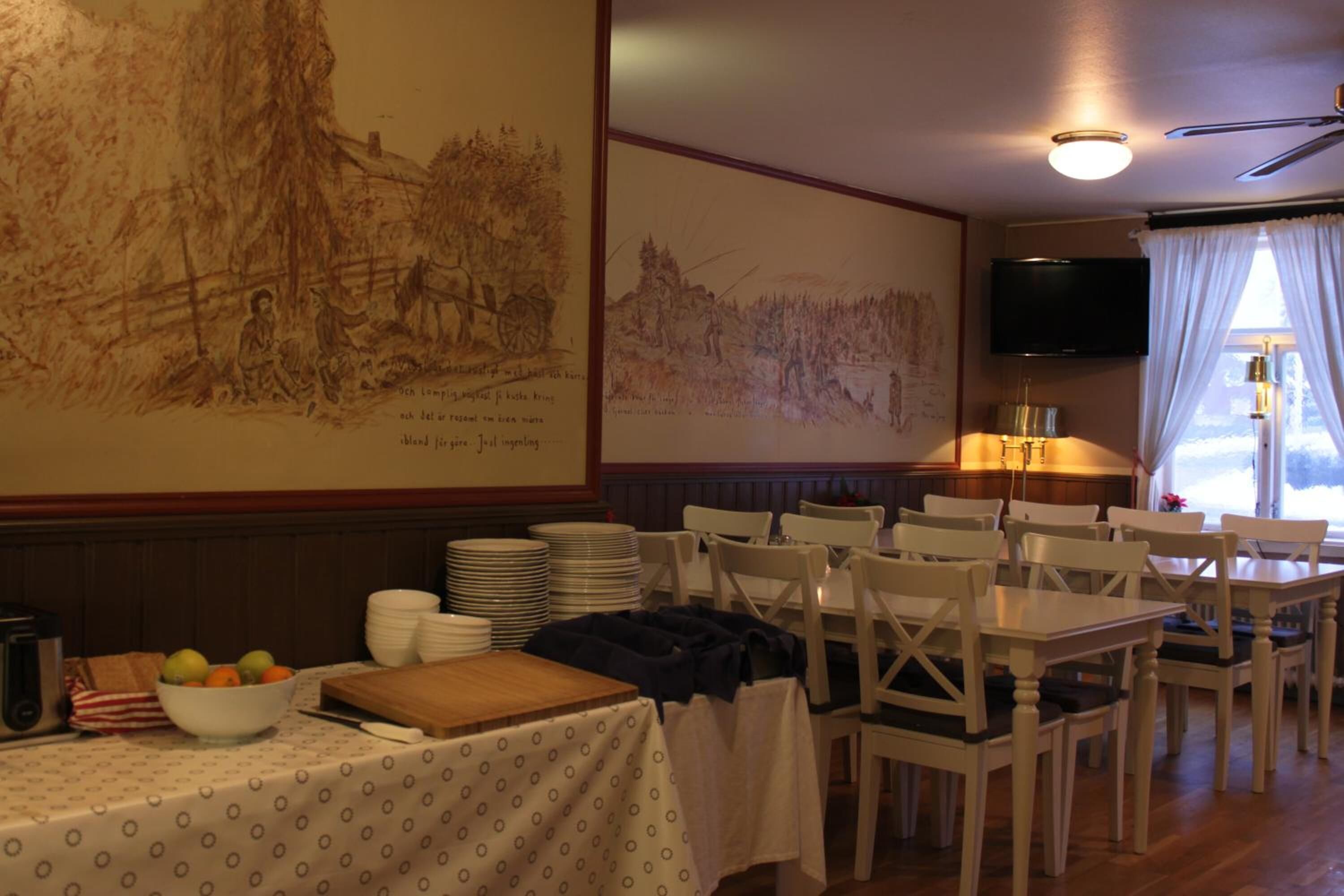 A dining area with tables and chairs, a large painting on the wall, and a television mounted above a window.