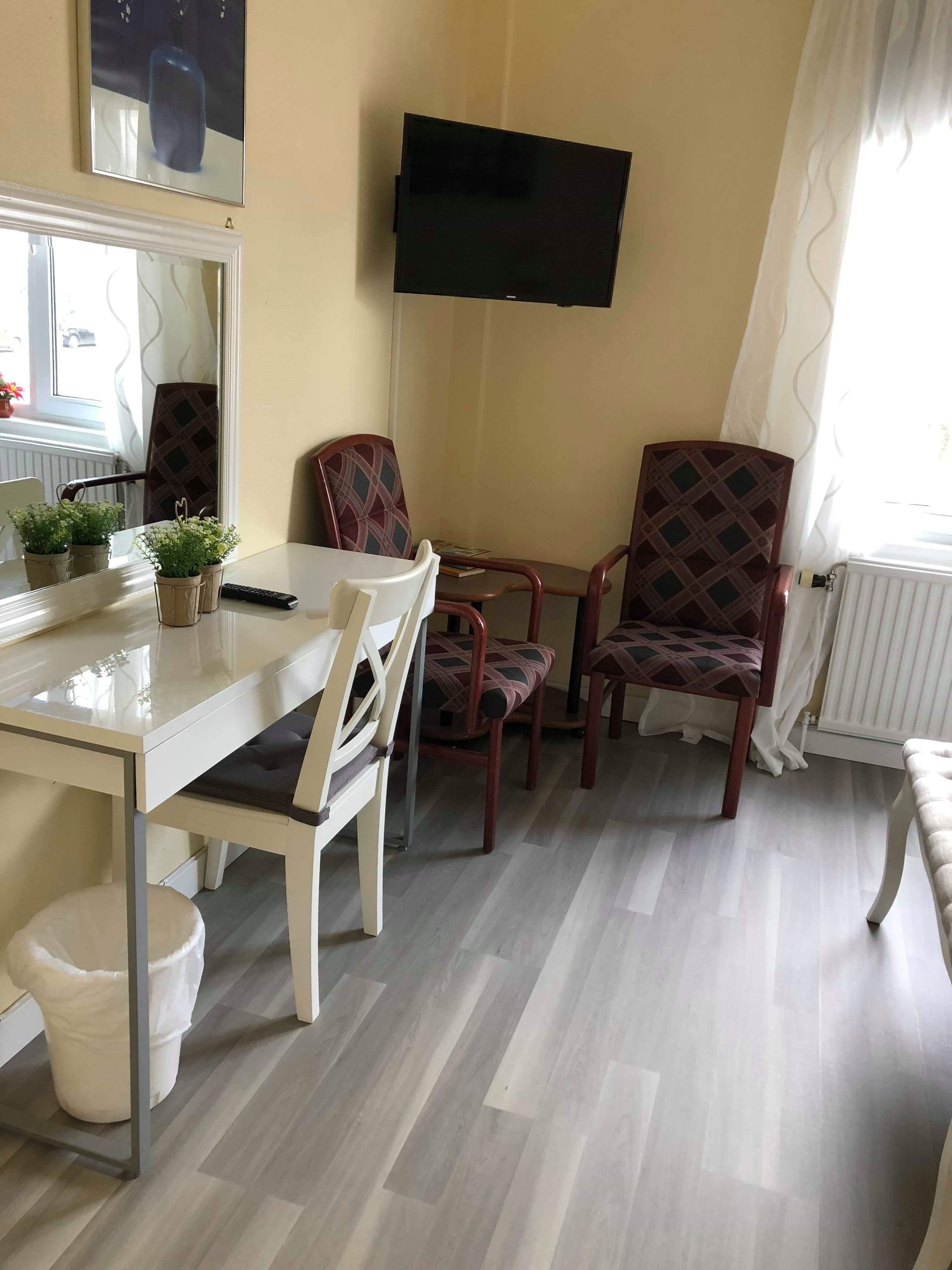 Un comedor con una mesa, sillas, un televisor montado en la pared y una ventana con cortinas.