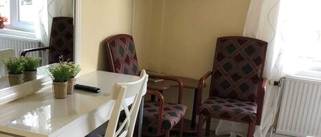 Un comedor con una mesa, sillas, un televisor montado en la pared y una ventana con cortinas.