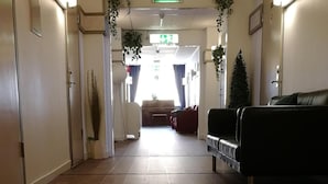 A hallway with a reception desk, a waiting area with a sofa, and a visible exit sign.