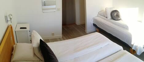 A hotel room with two beds, a bedside table with a lamp, a mirror, and a view of the hallway.