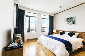 A hotel room with a large bed, a bedside table with a lamp, a window with curtains, and a painting on the wall.