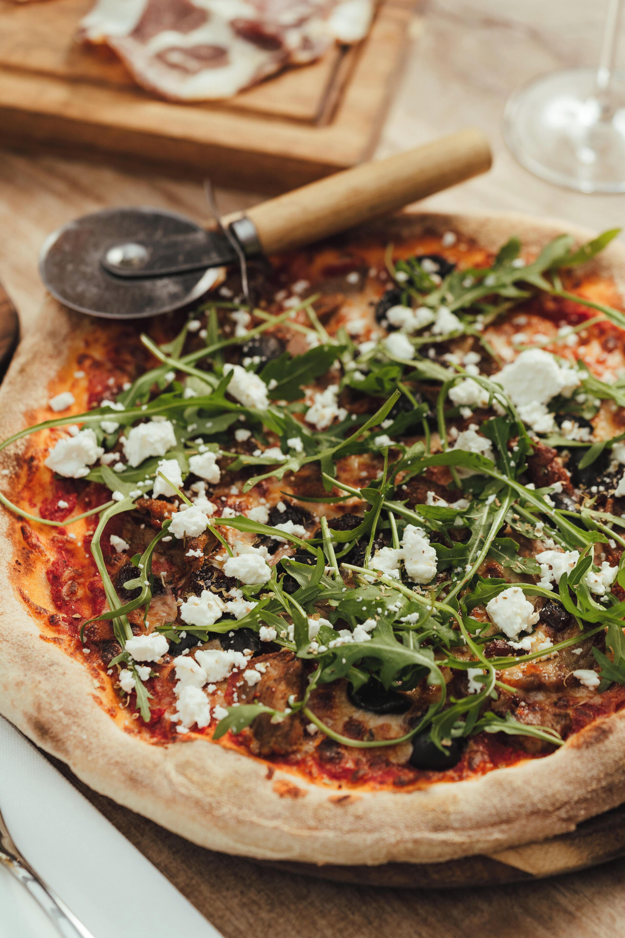 A pizza with toppings and a pizza cutter on a wooden surface.