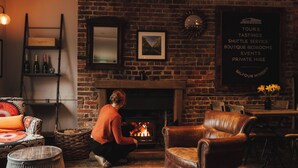 A cozy room with a brick wall, a fireplace, a sofa, a dining table, and a signboard listing services like tours and shuttle service. - Winemaker's Pub (Cranbrook)