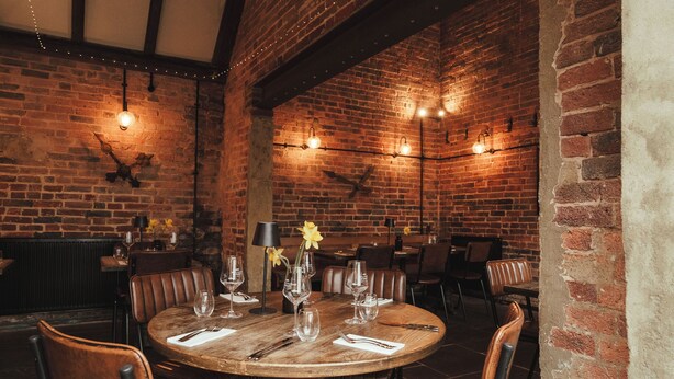 A brick-walled restaurant with round tables, leather chairs, and string lights. - Winemaker's Pub (Cranbrook)