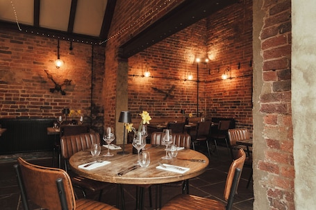 A brick-walled restaurant with round tables, leather chairs, and string lights.