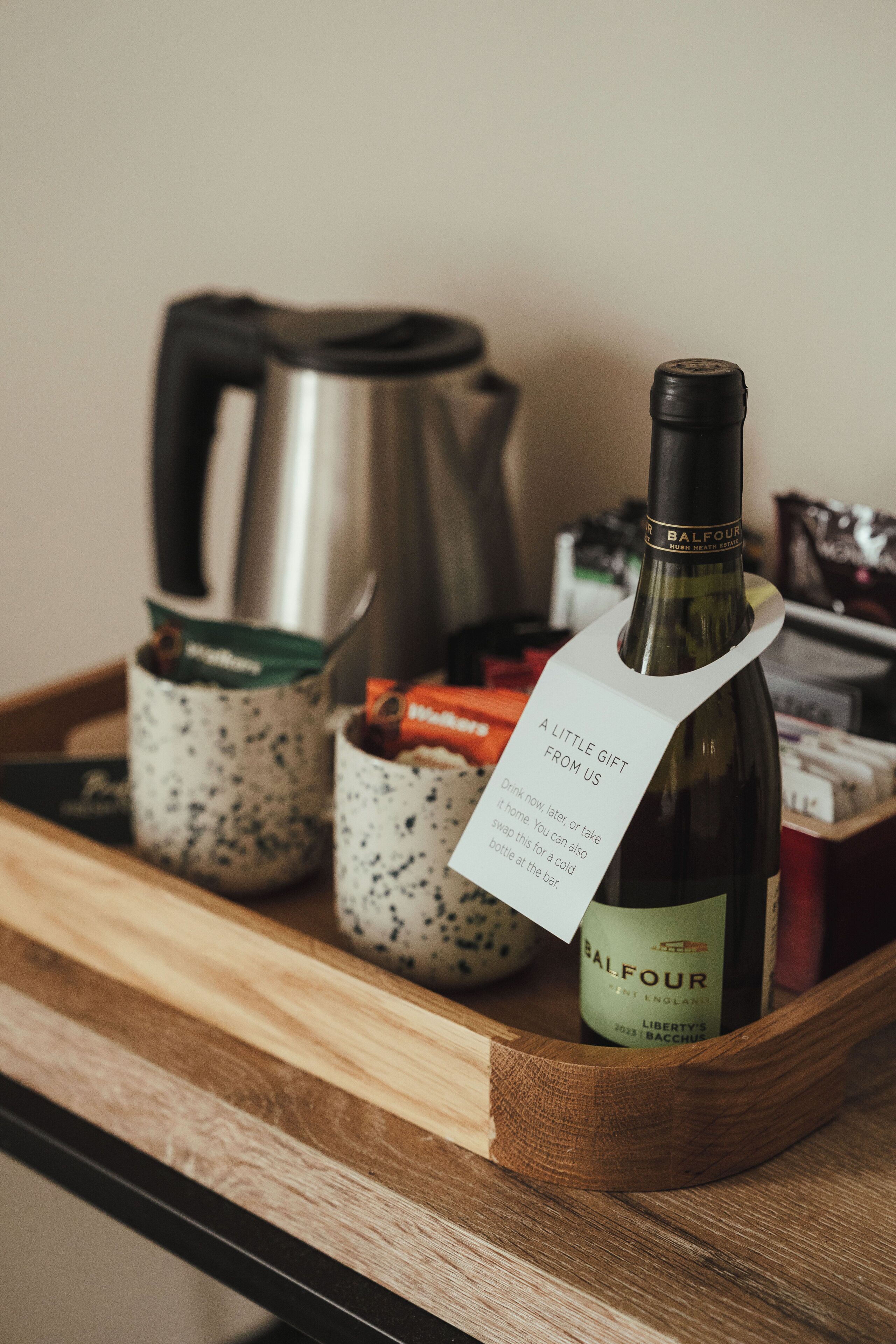 Een fles Balfour wijn met een tag, geplaatst op een houten dienblad met een waterkoker en kruidenpotjes.