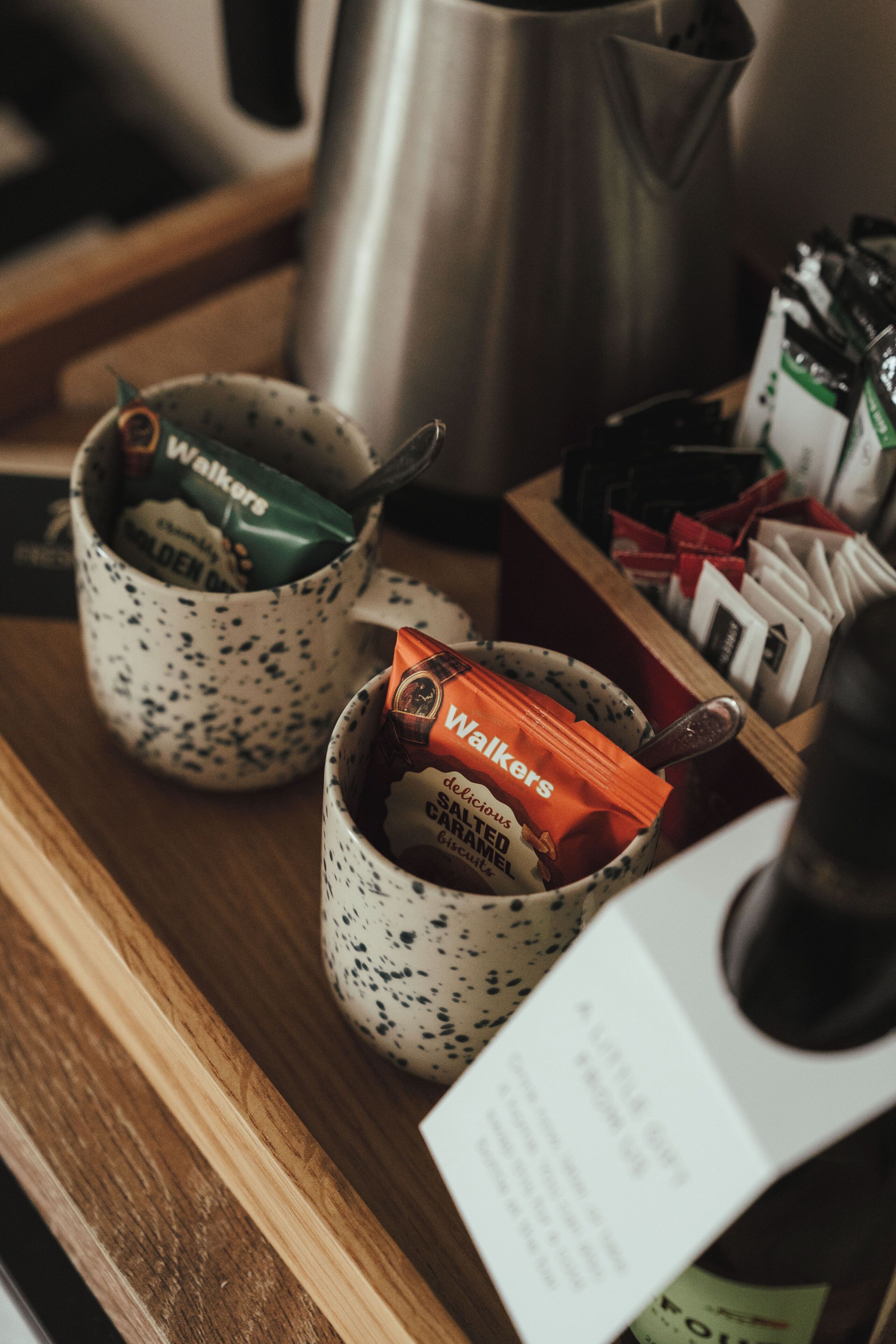 Two speckled ceramic mugs on a wooden surface, each containing a Walkers chocolate bar.