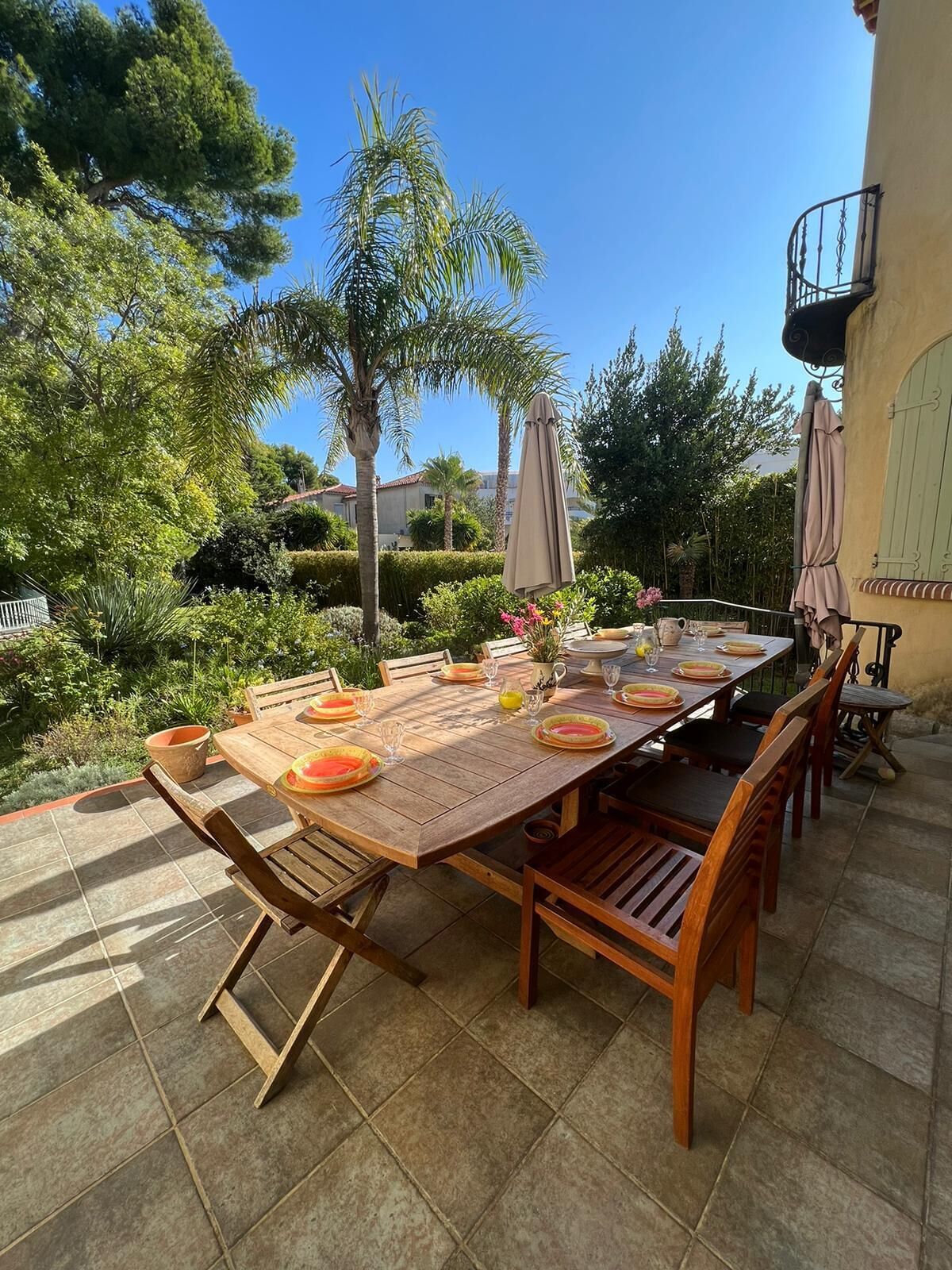 An outdoor dining area with a wooden table set for four, surrounded by chairs, and a large umbrella.