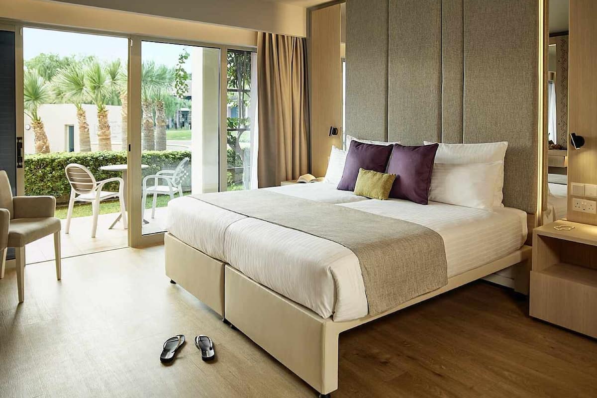 A modern hotel room with a large bed, a balcony with outdoor seating, and a view of palm trees.