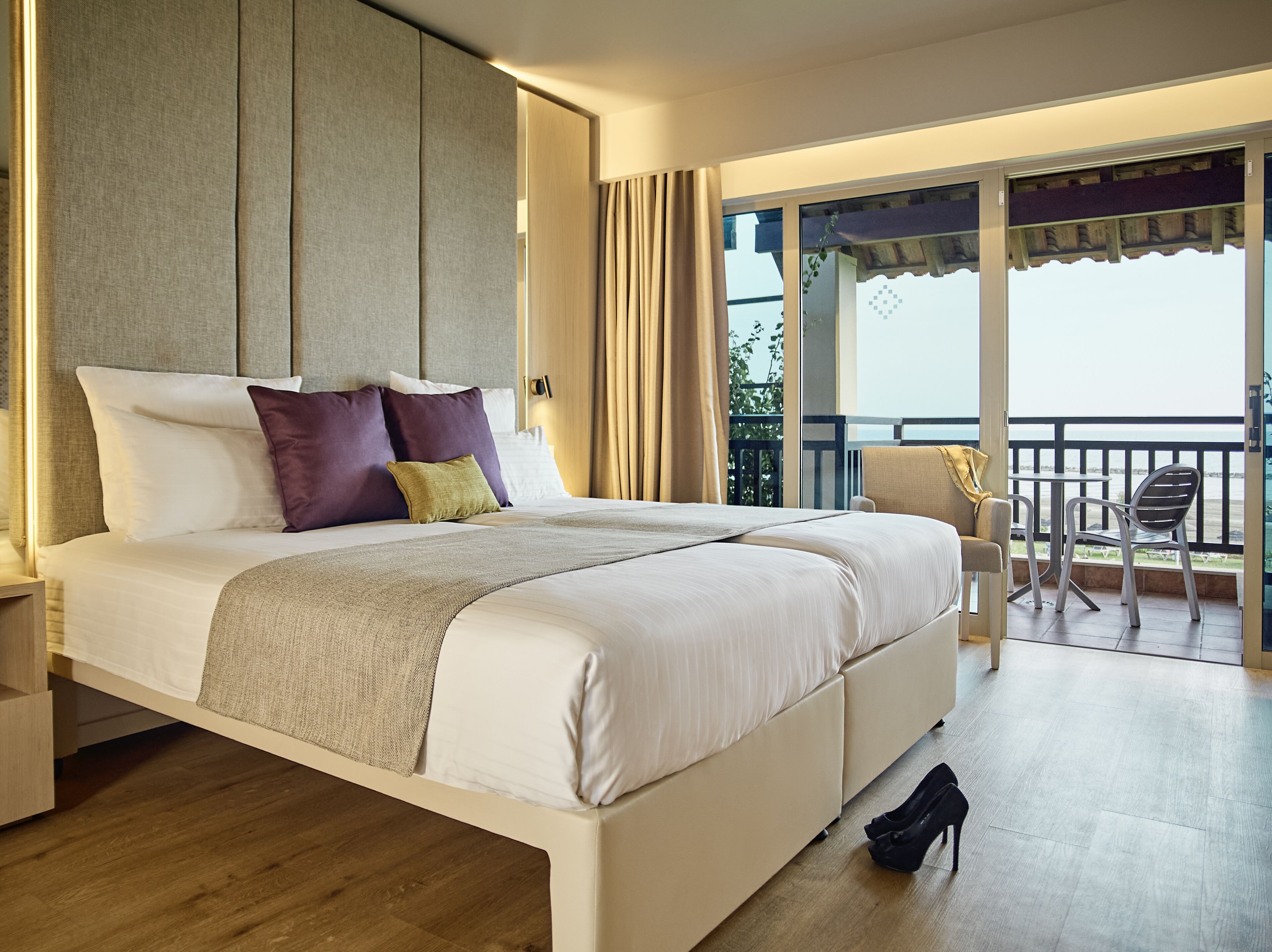 A modern hotel room with a large bed, a balcony with a view, and a small table with chairs.