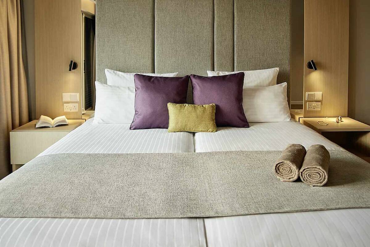 A neatly made bed with pillows, a bedside table with a book, and a wall-mounted light fixture.