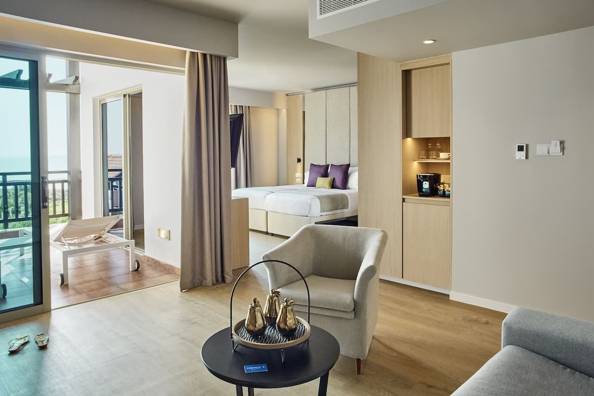 A modern hotel room with a balcony, a bed, a seating area, and a kitchenette.