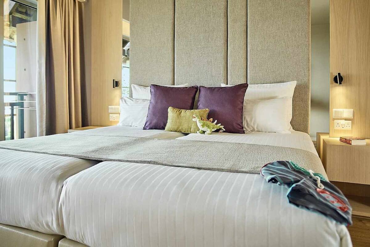 A hotel room with a large bed, a headboard, two bedside tables, and a window with curtains.