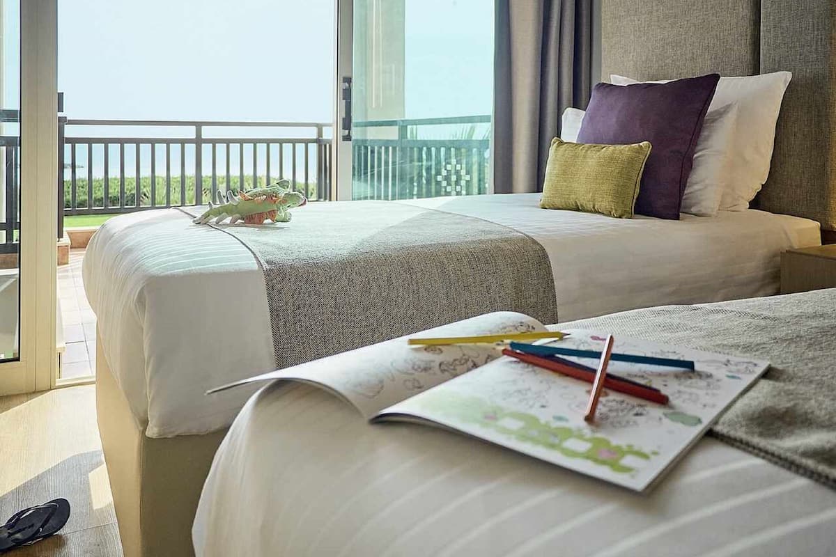 A hotel room with two beds, a balcony, and a view of the outdoors.