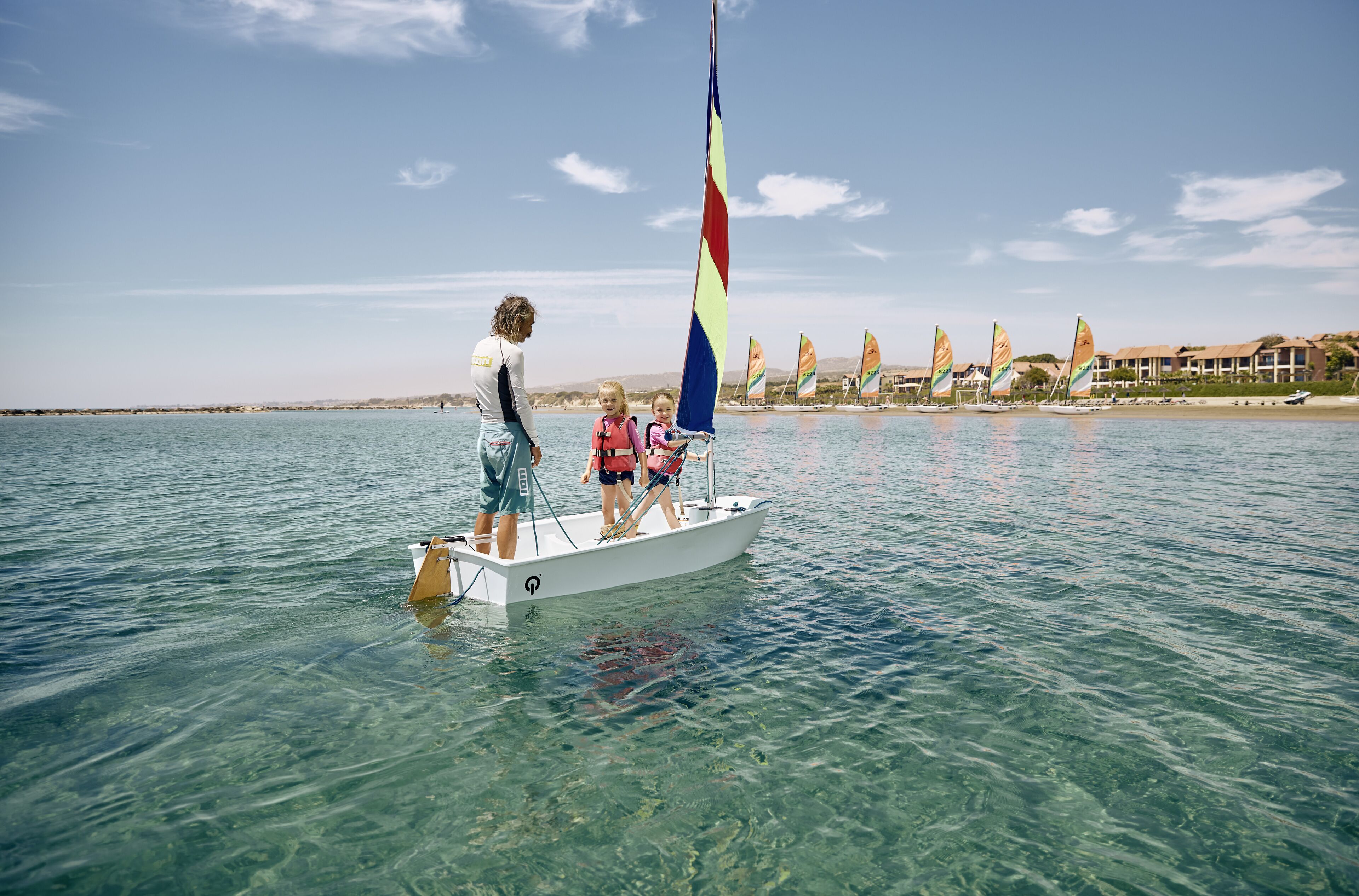 Un velero sobre aguas claras con una persona y dos niños a bordo.