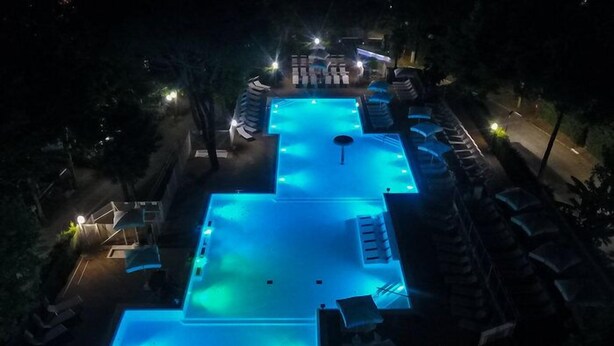 A swimming pool with lounge chairs and umbrellas, surrounded by trees and a well-lit area. - Camping Village I Tre Moschettieri (Comacchio)